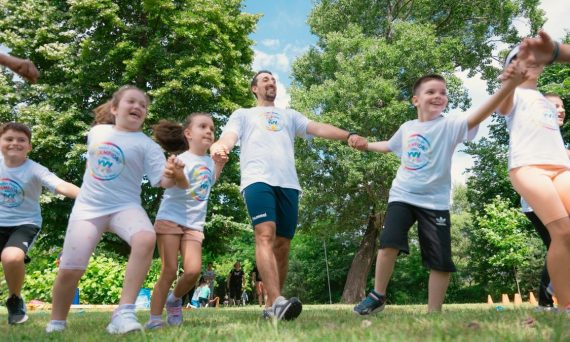 Group of joyful children playing outdoors with an instructor in a sunny park.
